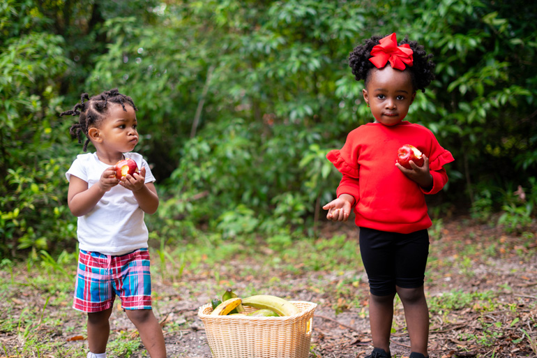 Deux fillettes d’origine haïtienne ou jamaïcaine s’amusent à l’extérieur en tenant chacune une pomme.