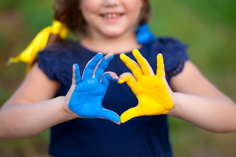 Une jeune fille sourit en formant un cœur avec ses mains peintes en bleu et jaune.